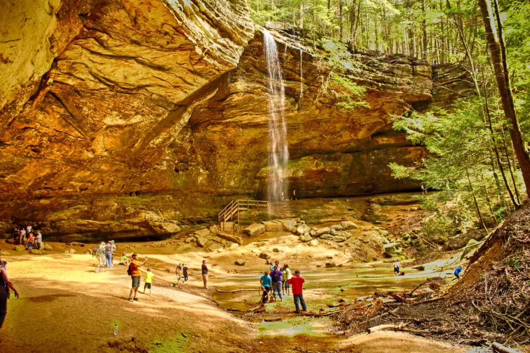 Visitors beneath the wide sandstone recess and thin waterfall at Ash Cave in Hocking Hills